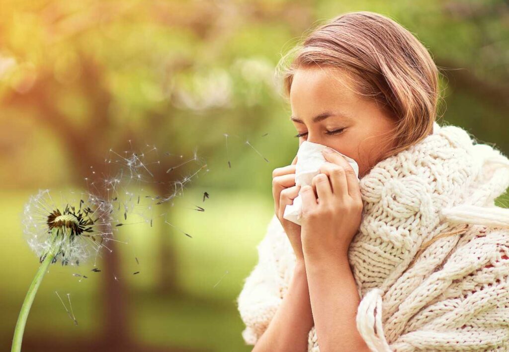 Woman in front of trees in the springtime blowing her nose.